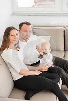 Parents and their beautiful baby girl sitting on the sofa and looking at the camera.
