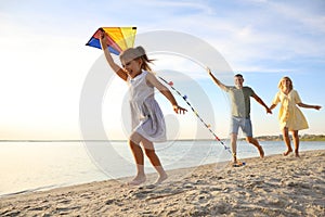 Happy parents with their child playing with kite on beach. Spending time in nature