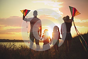 Parents and their children playing with kites outdoors at sunset, back view. Spending time in nature