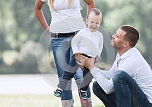 Parents and their little son playing with the ball on the lawn.