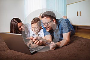 Parents and their son are doing shopping online using laptop and smiling at home