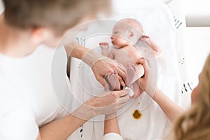 Parents together cahnging nappy to newborn son who is lying on changing mat at home.