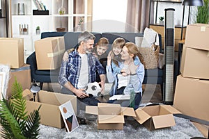 Parents with two kids sitting among boxes at new flat