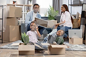 Parents unpacking boxes while kids playing at new flat