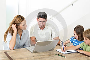 Parents using laptop while children coloring