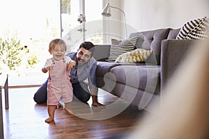 Parents Watching Baby Daughter Take First Steps At Home