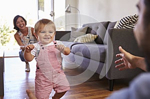 Parents Watching Baby Daughter Take First Steps At Home