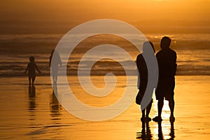 Parents watching kids silhouettes at sunset on beach