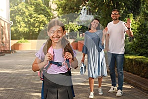 Parents waving goodbye to their daughter before school outdoors