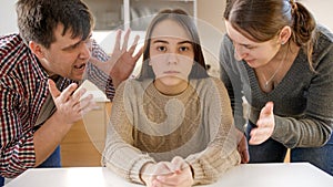 Parents yelling and shouting at teenage daughter sittin behind table and looking in camera