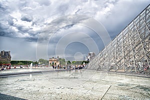 Paris, France - June 02, 2017: courtyard of Louvre Museum with glass pyramid and people queue on cloudy sky. Landmark of french ca