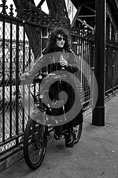 PARIS, FRANCE - MAY 04, 2023: Curly-haired girl in a black leather jacket rides a bike in Paris