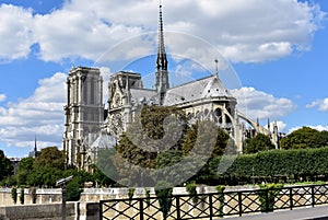 Paris, France. Notre Dame Cathedral from bridge over Seine river. Trees and river walk. Blue sky with clouds.