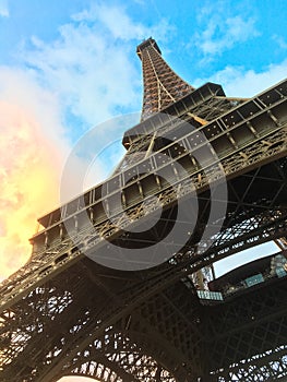 Paris`s Eiffel Tower from a ground level perspective against blue and yellow sunset clouds