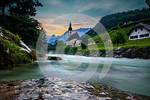 The parish church of St. Sebastian in Ramsau near Berchtesgaden as a long exposure with the river and a bridge at sunset