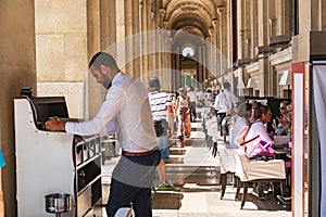 Parisians and tourists enjoy summer day drinks in cafe on a terrace of Louvre