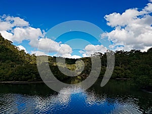 Beautiful morning view of a creek with reflections of deep blue sky, light clouds, mountains and trees