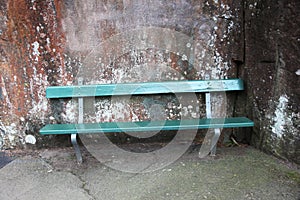 Park bench in green against a natural stone wall