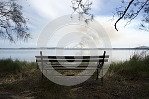 Park bench on lake edge with a view of a bushfire, Central Coast of NSW, Australia