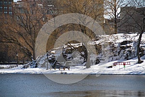 Park bench next to lake, cliff and trees with snow in winter