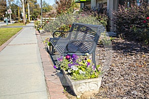 A park bench next to a side walk with colorful flowers