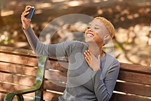 Park bench, phone selfie and black woman in nature outdoors taking picture. Happy, smile and girl from South Africa with