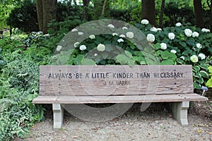 A park bench with a quote from J.M. Barrie engraved on it in front of blooming hydrangea bushes in a park in Wisconsin