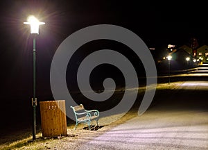 Park bench and trash container illuminated by a lantern