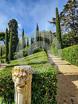 Park in English style. Antique column with a lion\'s head. Cypress trees, pines and green lawns. Spring.