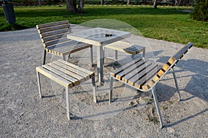 Park furniture chess table and chairs for four persons made of light metal and wooden beams with backrest on bright glade area gra