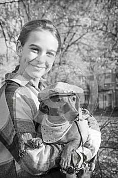 In the park, a girl holds a dachshund dog in her arms. Black and white photo