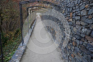 In the park there is a path under the terraces of gray stone and railings in the shape of gates. Trellis for climbing roses. Forge