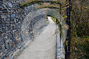 In the park there is a path under the terraces of gray stone and railings in the shape of gates. Trellis for climbing roses. Forge