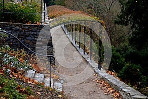 In the park there is a path under the terraces of gray stone and railings in the shape of gates. Trellis for climbing roses. Forge