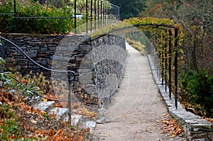 In the park there is a path under the terraces of gray stone and railings in the shape of gates. Trellis for climbing roses. Forge