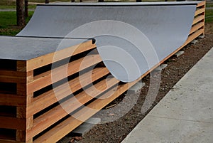 In the park there is a skateboard ramp in the shape of the letter u. Large construction of wooden beams and a metal surface. young