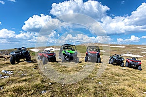 Parked ATV and UTV, buggies on mountain peak with clouds and blue sky in background