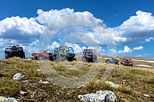 Parked ATV and UTV, buggies on mountain peak with clouds and blue sky in background
