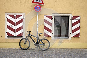 Parked bike to the wall of the house and a road sign â€™No stopping