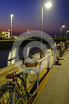 Parked bikes in the harbor of Senigallia, Italy at night. Lights, street lamps, and water reflecting in the city