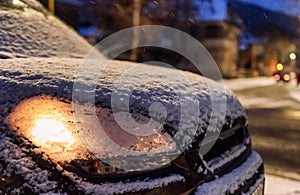 Parked car with light on covered by snow at night