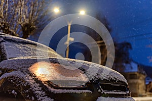 Parked car with light on covered by snow at night