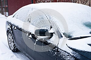 Parked modern dark colored car covered with snow in winter season