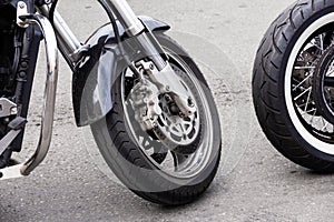 Parked motorcycle wheels/ Close-up of the front wheel of a motorcycle and brake disc. Chrome fork and black motorbike wing