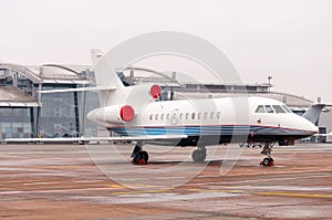 Parked private airplane on the runway near airport terminal. white civic, modern jet