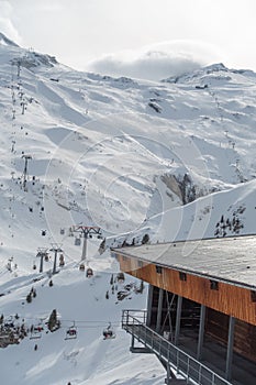 Parked ski cabins, gondolas in a wooden big house, and a ski piste in distance
