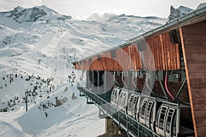 Parked ski cabins, gondolas in a wooden big house, and a ski piste in distance