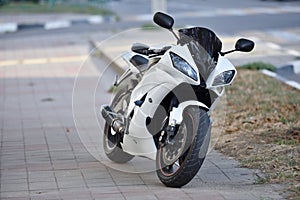 A parked sports bike is standing on the sidewalk in the city. The sports motorcycle is black and white