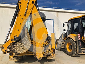 Parked yellow backhoe loader. Earthmoving, excavating, digging machinery at construction site