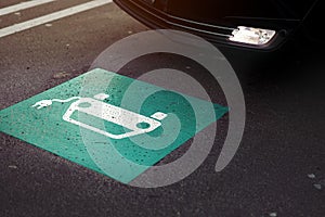 parking lot scene with car entering a section marked with symbol of a car with cable plug painted on ground.